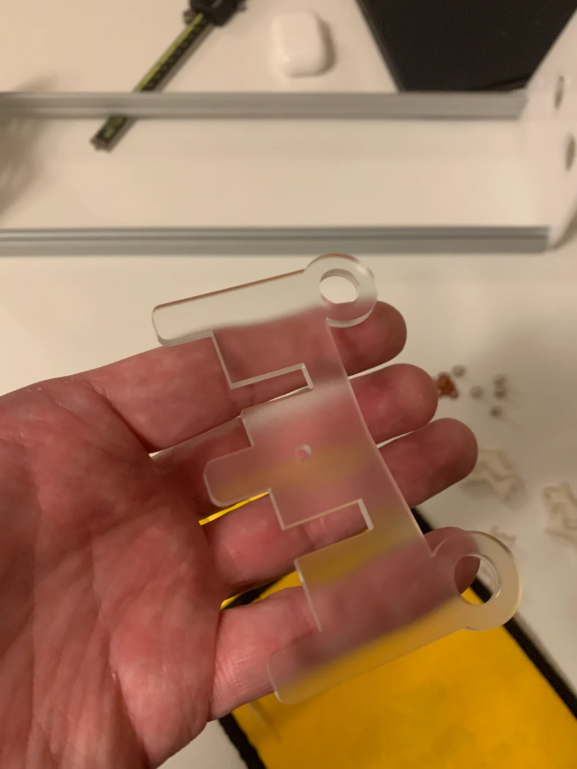 A hand holding a flat clear-acrylic case panel with finger-jointed edges, fresh off the laser.